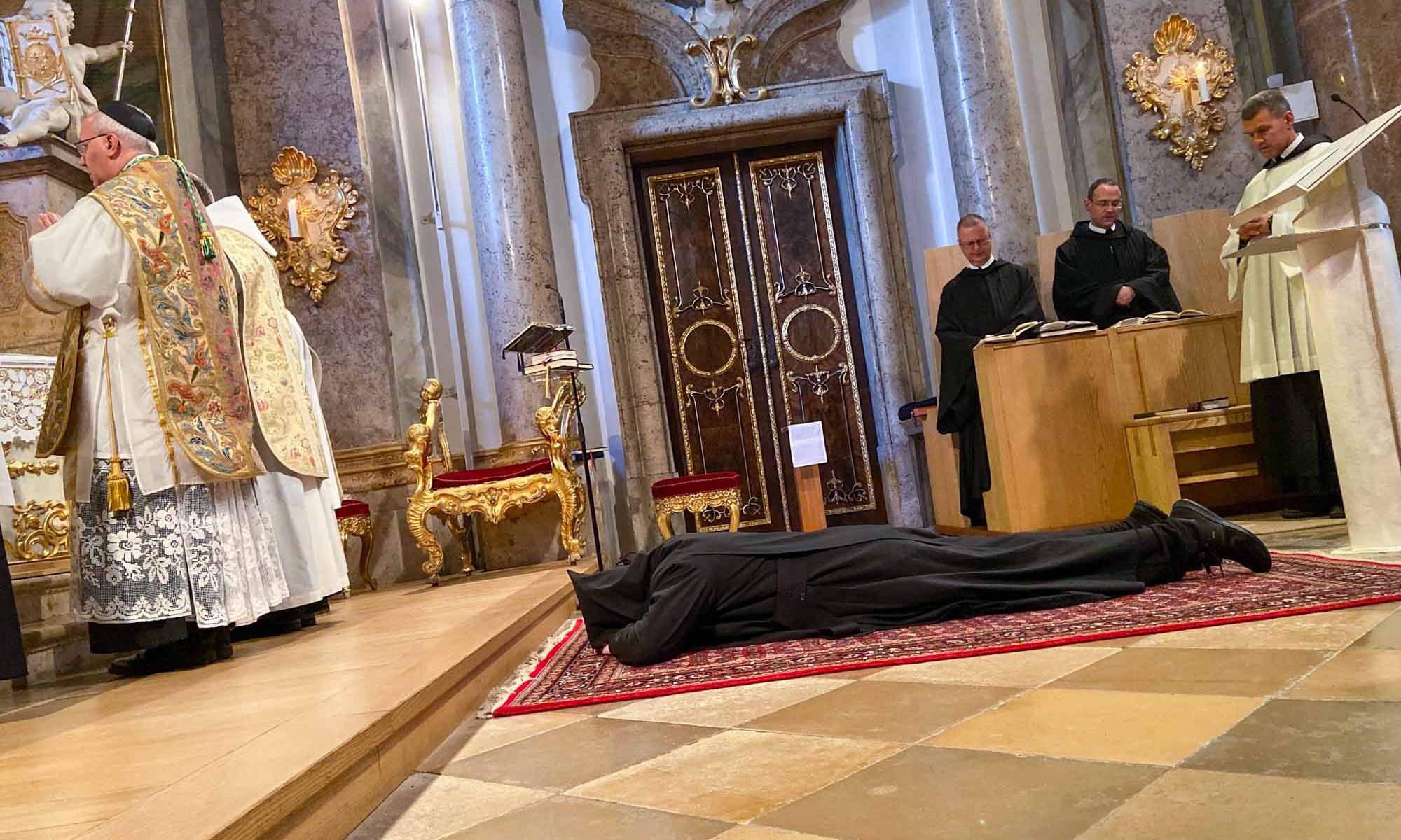 Mönch liegt auf einem Teppich im Presbyterium der Abteikirche St. Georg zu Weltenburg während der Heiligenlitanei
